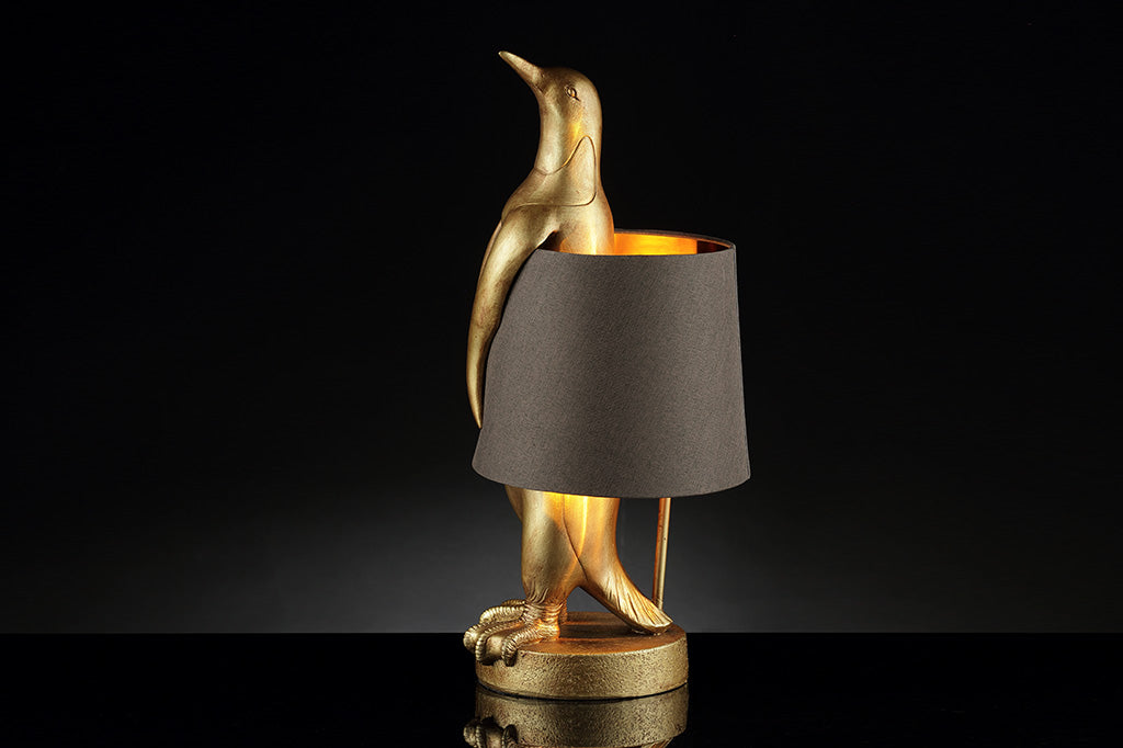 face left view of whimsical table lamp of gold finished resin penguin wearing a brown fabric lampshade around its torso.