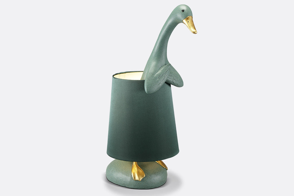 whimsical table lamp, resin. Green duck wearing a lampshade around its torso with gold webbed feet sticking out on lamp base.