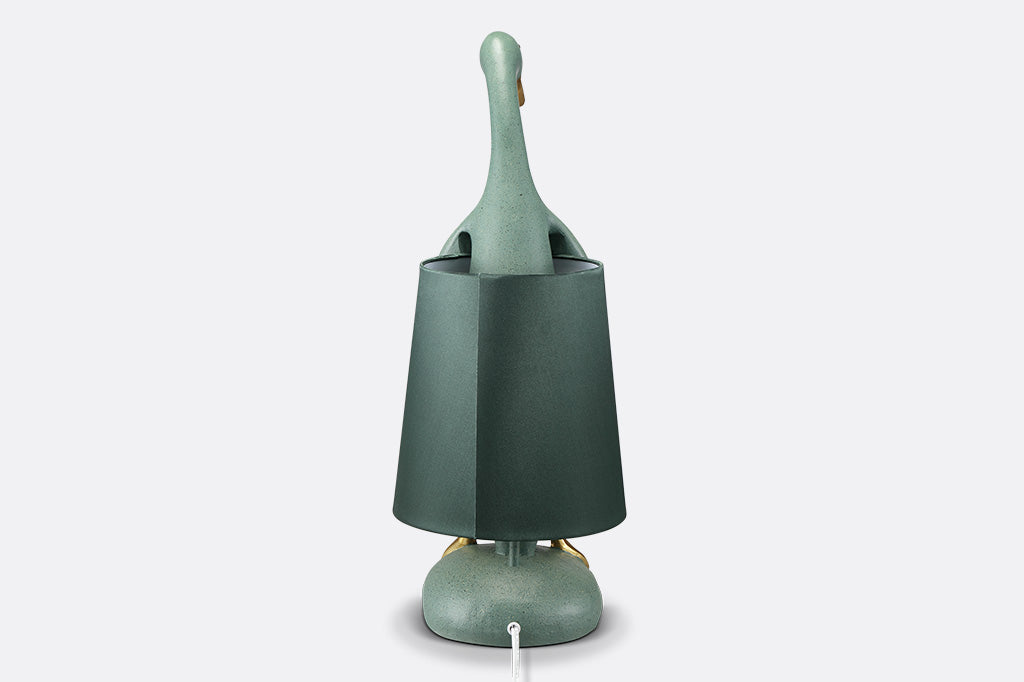 back view of whimsical table lamp, resin. Green duck wearing a lampshade around its torso with gold webbed feet sticking out on lamp base.