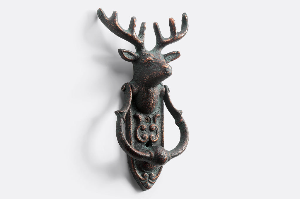 cast metal deer head with antlers and a horseshoe shaped knocker on rounded rectangle metal plate doorknocker face right 