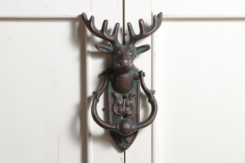 cast metal deer head with antlers and a horseshoe shaped knocker on rounded rectangle metal plate doorknocker 