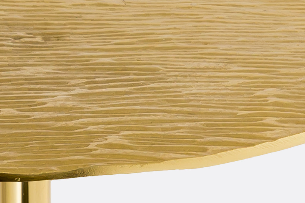 Close-up of a gold metallic surface with a textured pattern on a gold cast metal accent table with white marble base.
