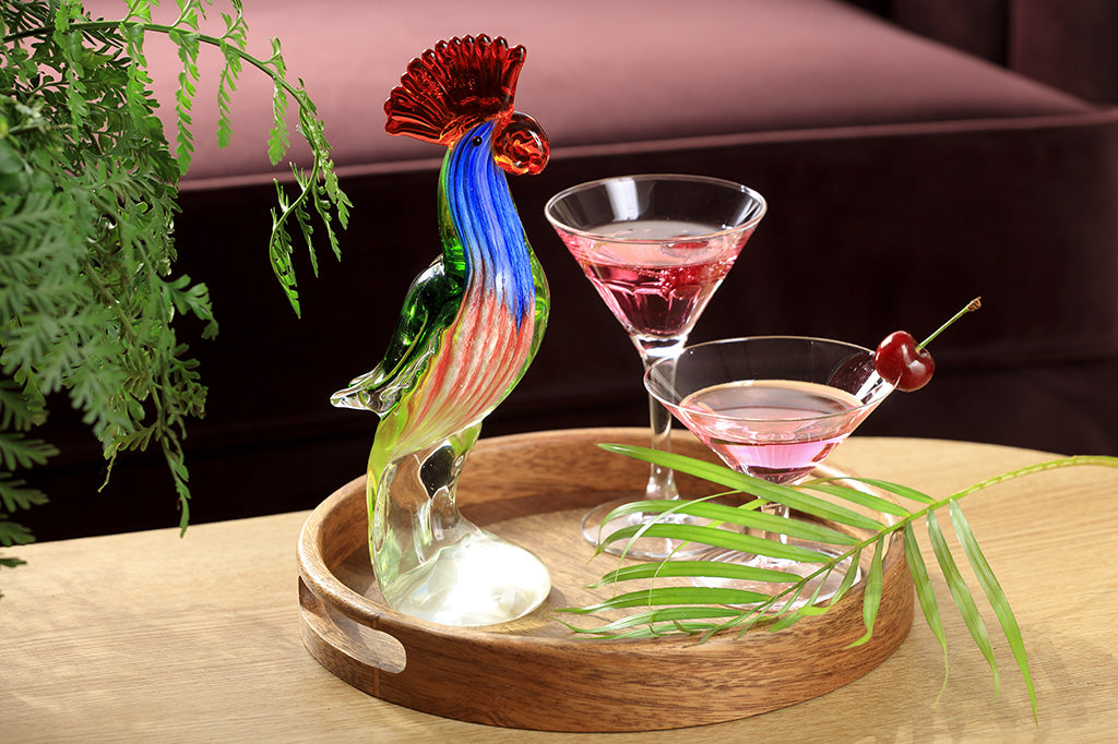tropical parrot glass sculpture decor shown among tropical foliage on a coffee table