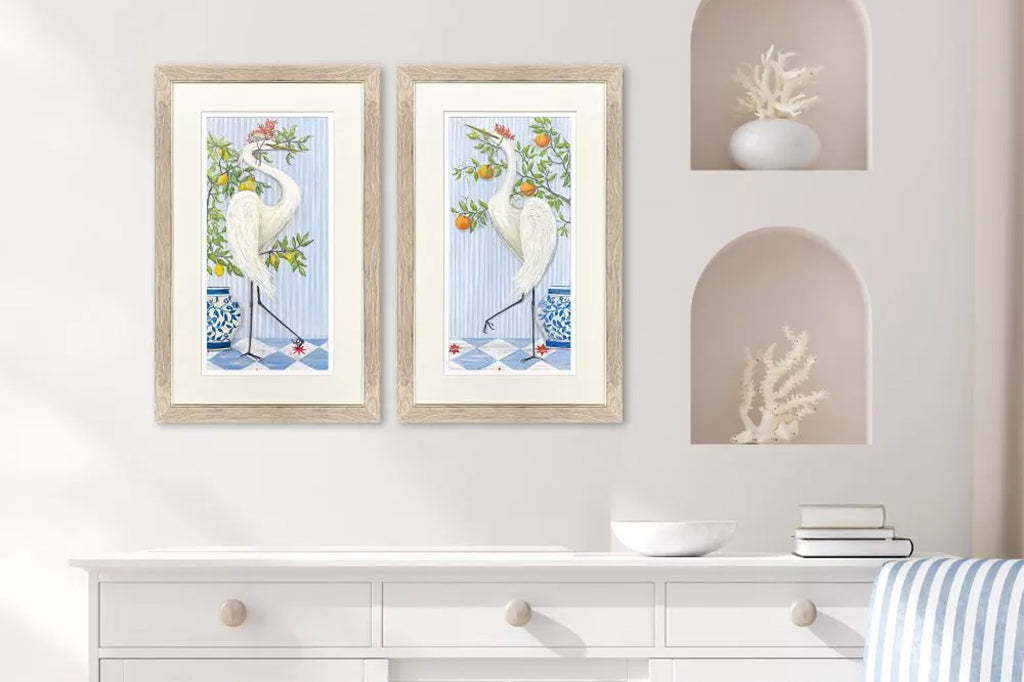 Framed artwork of cranes wearing crowns made of coral next to fruit trees.