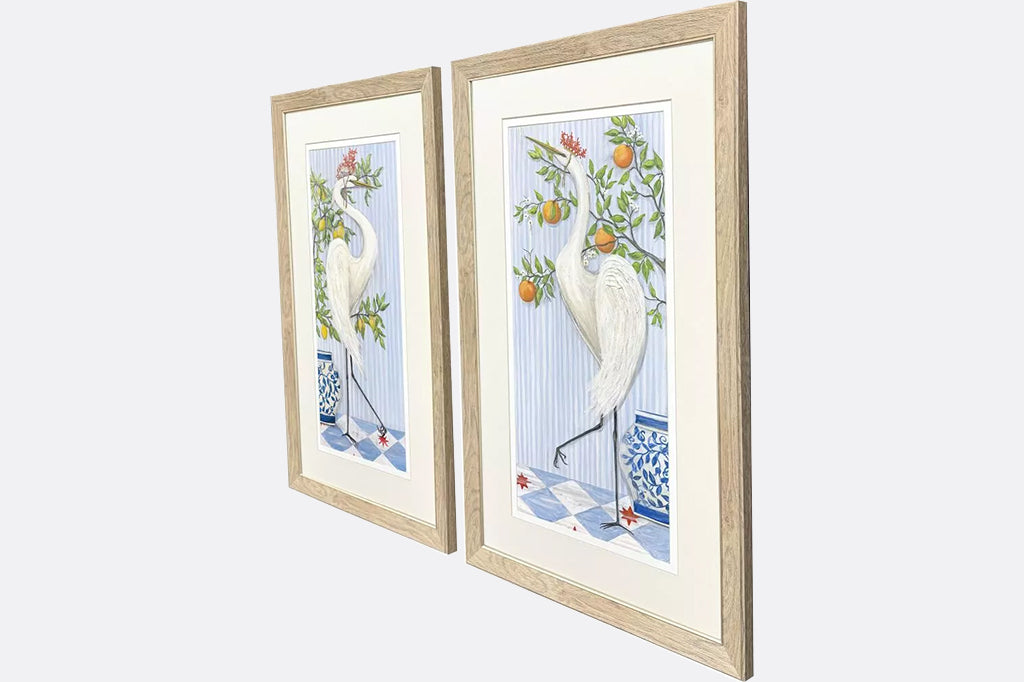 Framed artwork of cranes wearing crowns made of coral next to fruit trees.