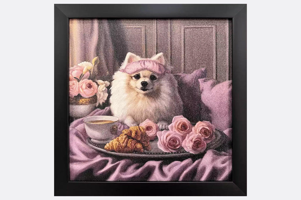Framed artwork of a dog wearing a pink sleeping mask with a coffee cup, croissant, and flowers on a bed.