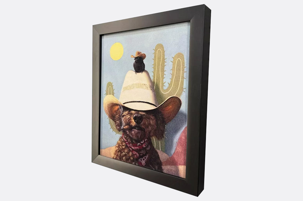 Framed artwork of a dog wearing a cowboy hat and a bird wearing a cowboy hat on top of him with a cactus and sun in the background.