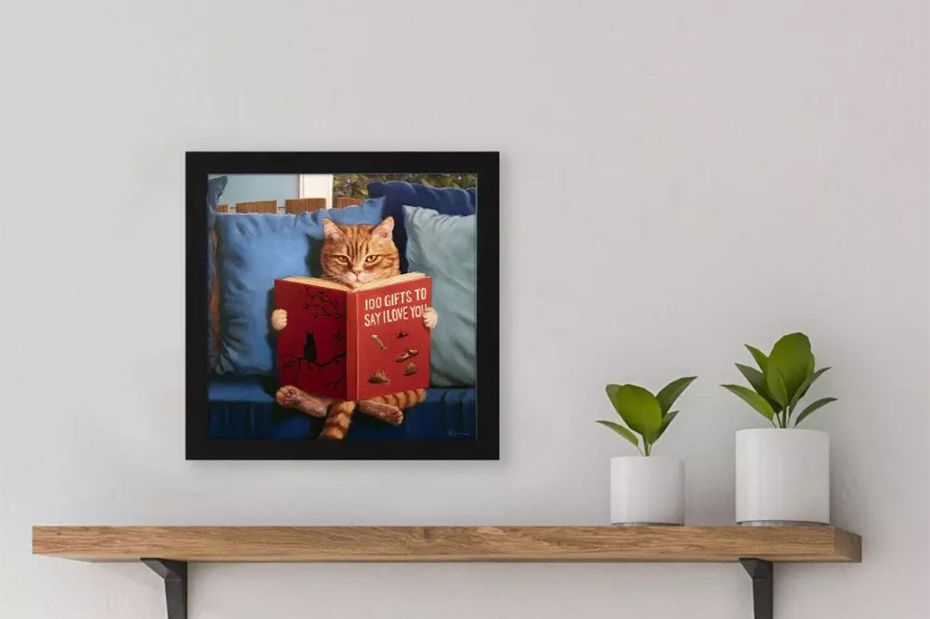 Cat sitting on a couch reading a book titled '100 Gifts to Say I Love You'.