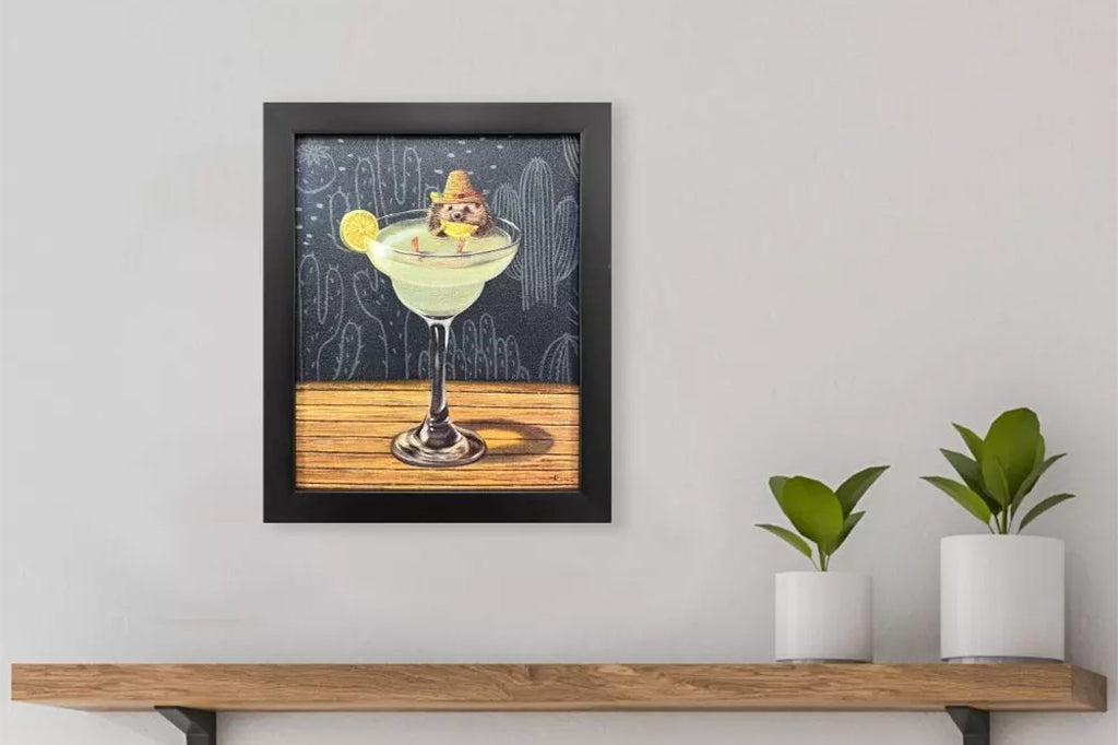 Framed artwork of a hedgehog wearing a sombrero sitting inside of a margarita glass with a cactus background.