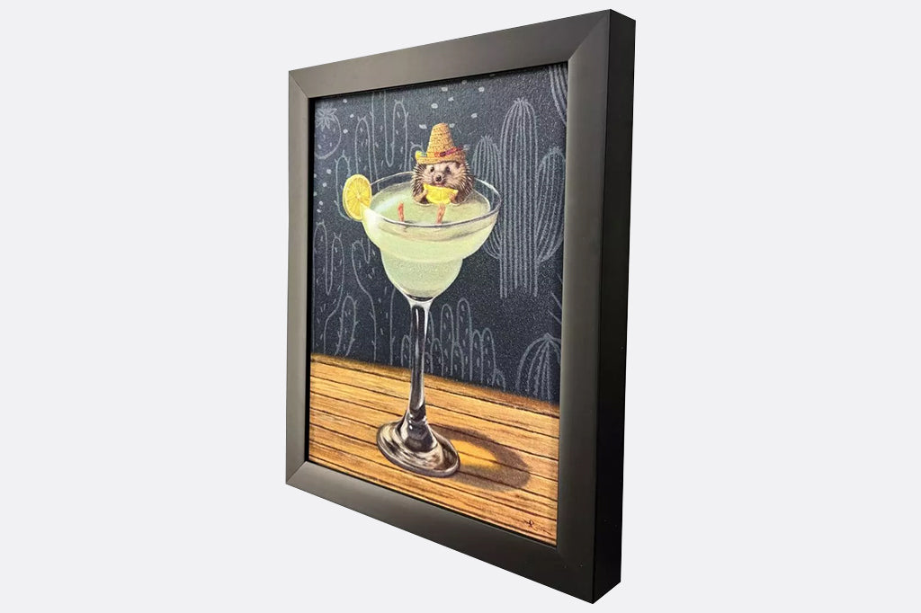 Framed artwork of a hedgehog wearing a sombrero sitting inside of a margarita glass with a cactus background.