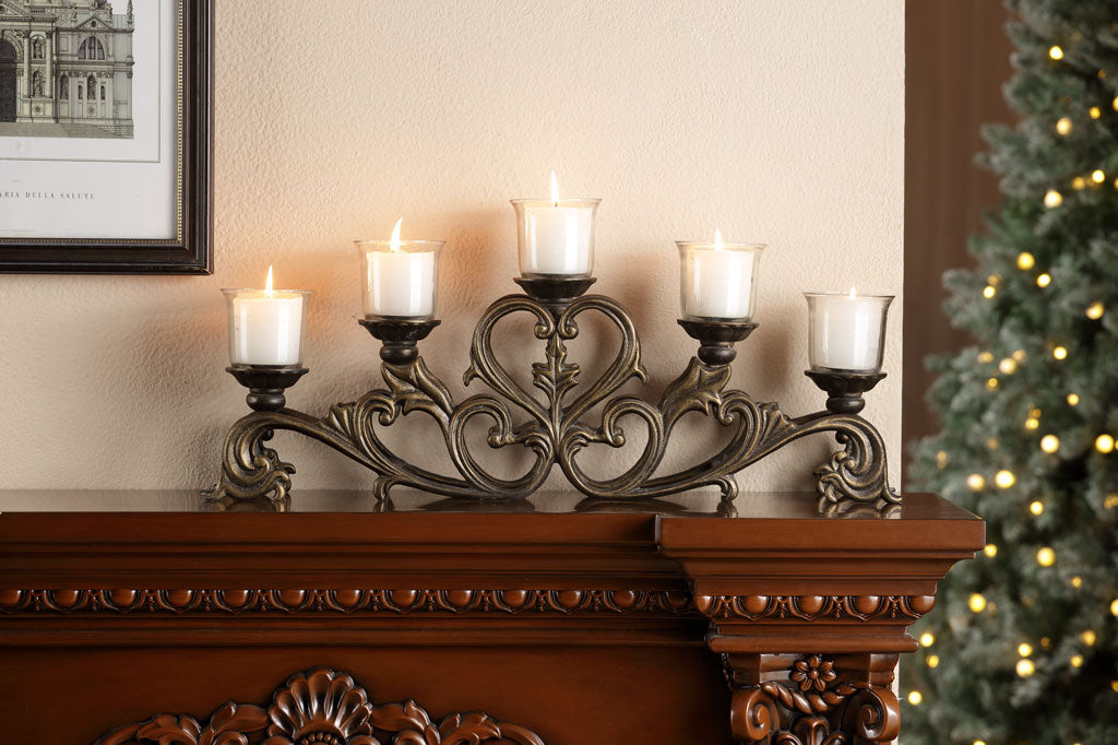 Decorative candle holder with lit candles on a wood mantel next to a Christmas tree.