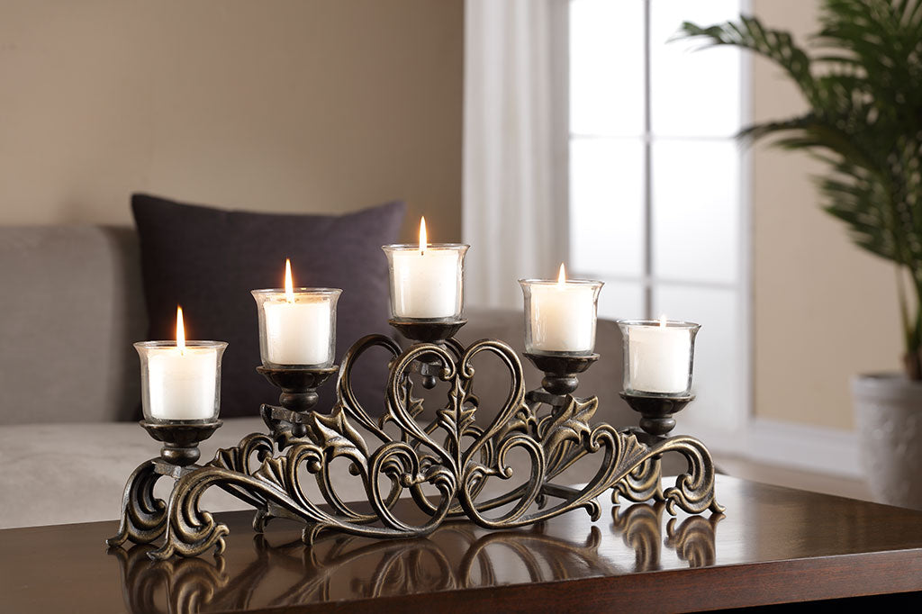 Candelabra with scrollwork and heart motif shown with 5 lit candles while on a wood table in living room