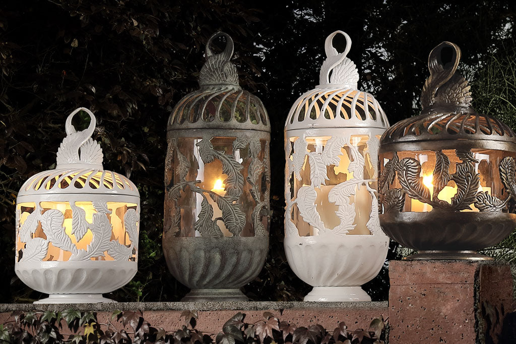 Four decorative lanterns with intricate feather designs and lit candles inside, set against a dark background.