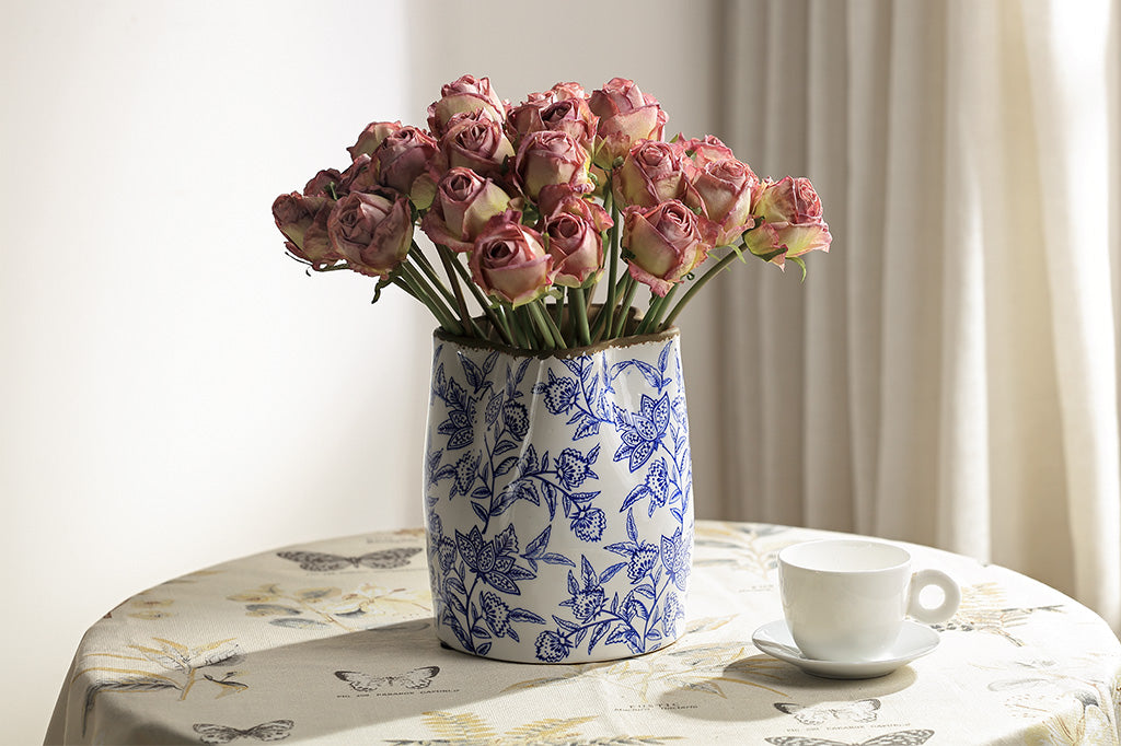 Bouquet of pink roses in a blue and white patterned vase on a table with a tea cup.