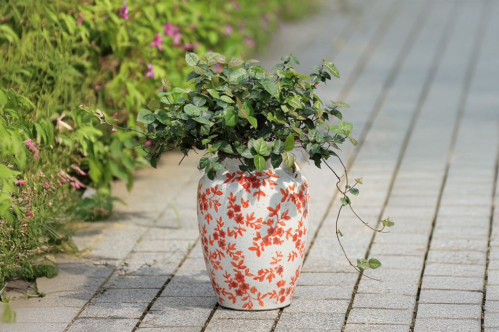 A white vase with orange flowers and leaves.