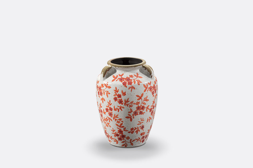 A white vase with orange flowers and leaves.