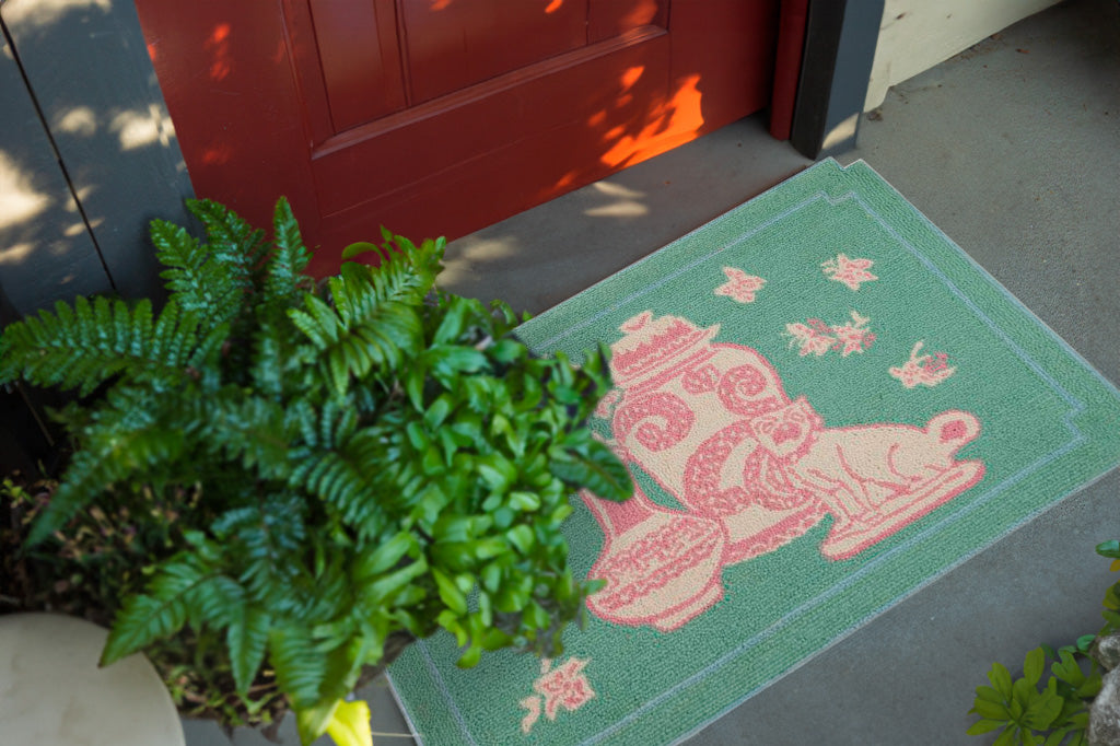 Chic Chateau hooked wool doormat/rug with notched corners, chinoiserie imagery in pastel green and pink, shown in front of apartment doorway by potted plants