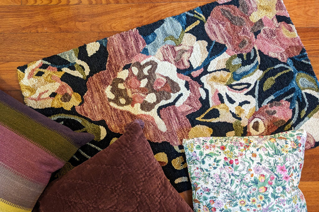 hooked rug with scattered blossom print shown on floor with a variety of scattered throw pillows