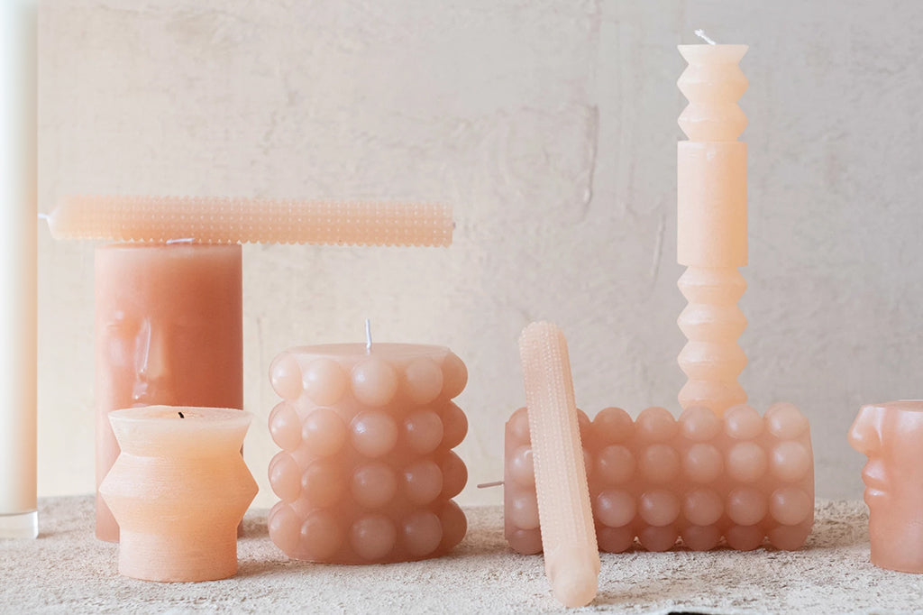 Collection of pink taper and pillar candles against textured wall background 
