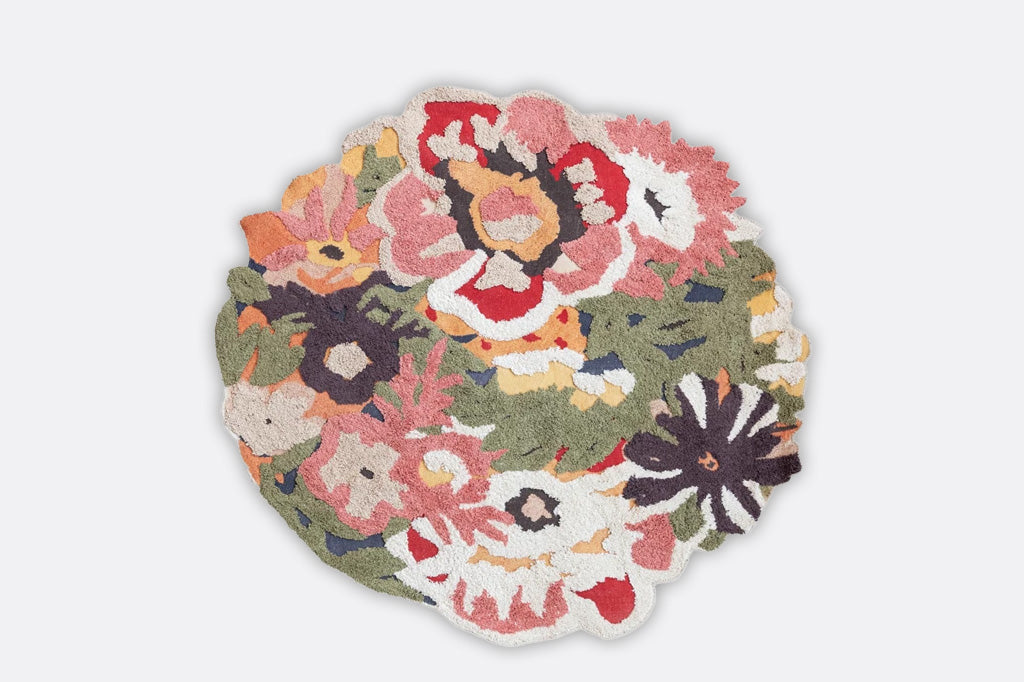 tuffed circular rug with floral and leaf motifs. Rug has splashes of pink, red, white, and green florals 