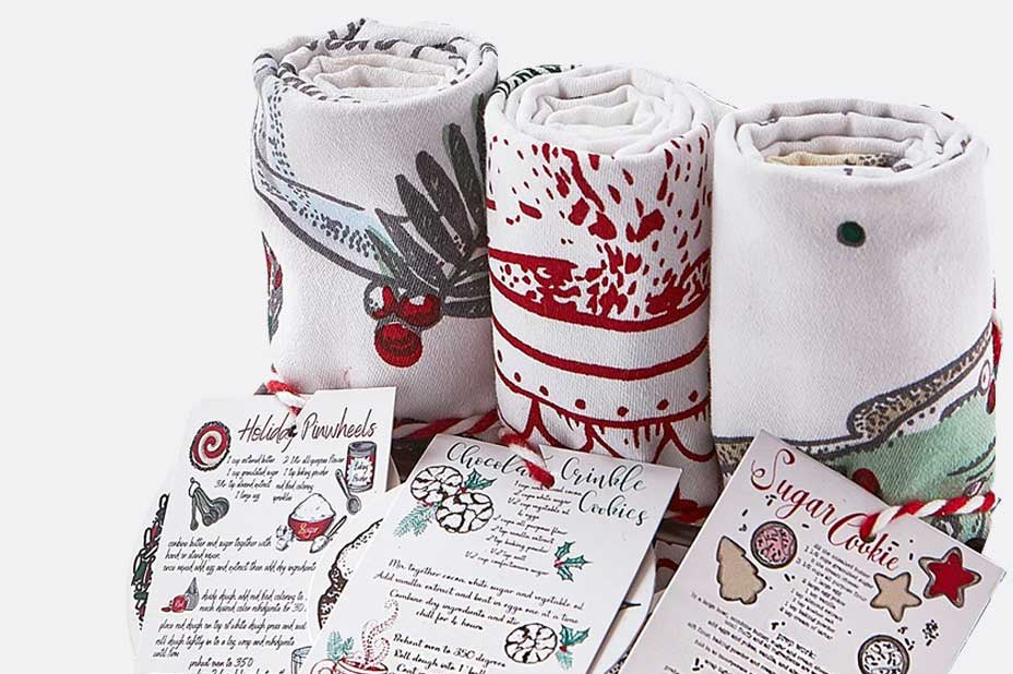 tea towels with holiday cookie theme shown rolled up with red cord and recipe card