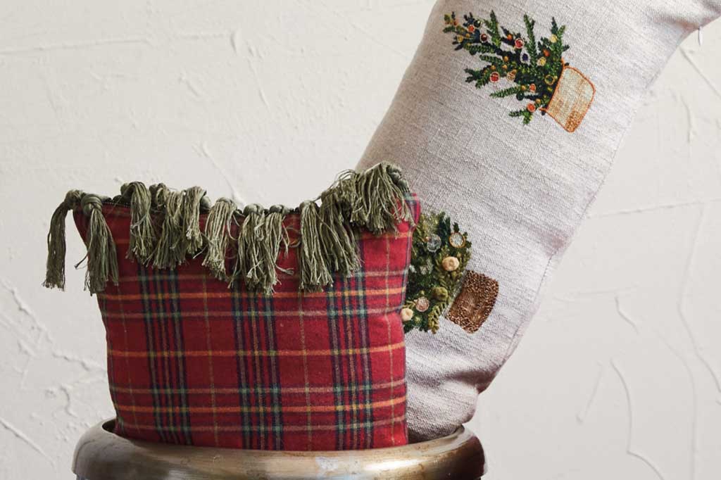 close up view of red tartan plaid lumbar throw pillow with green tassel fringe, shown in storage bin with other pillow
