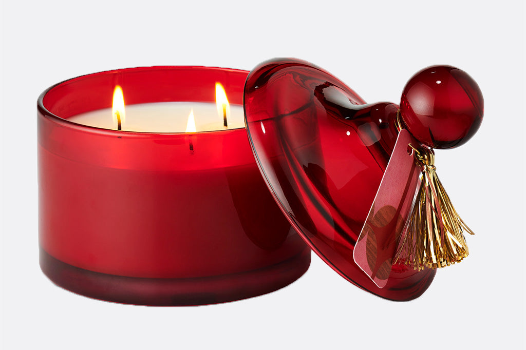 Red glass lidded candle shown with 3 lit wicks and gold tassle tag