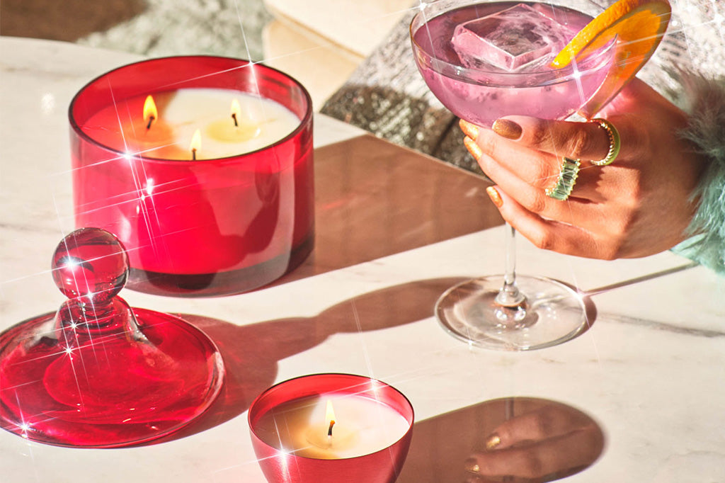 Enhanced photo shows sparkles on red glass candle on a table set with pink martini  held by manicured hand