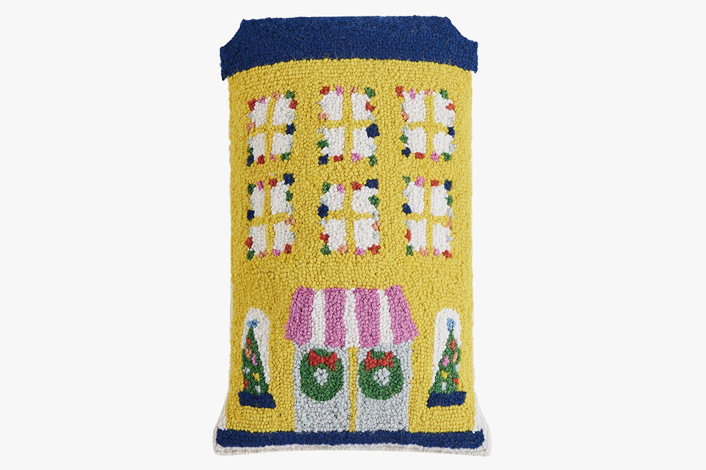 hooked wool pillow features a charming, shaped yellow hotel adorned with festive holiday lights