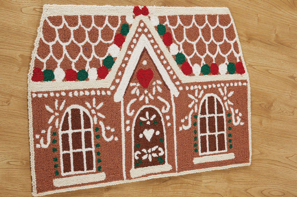 Hooked rug in shape of gingerbread cookie house with icing and gumdrop motif, shown on wood floor