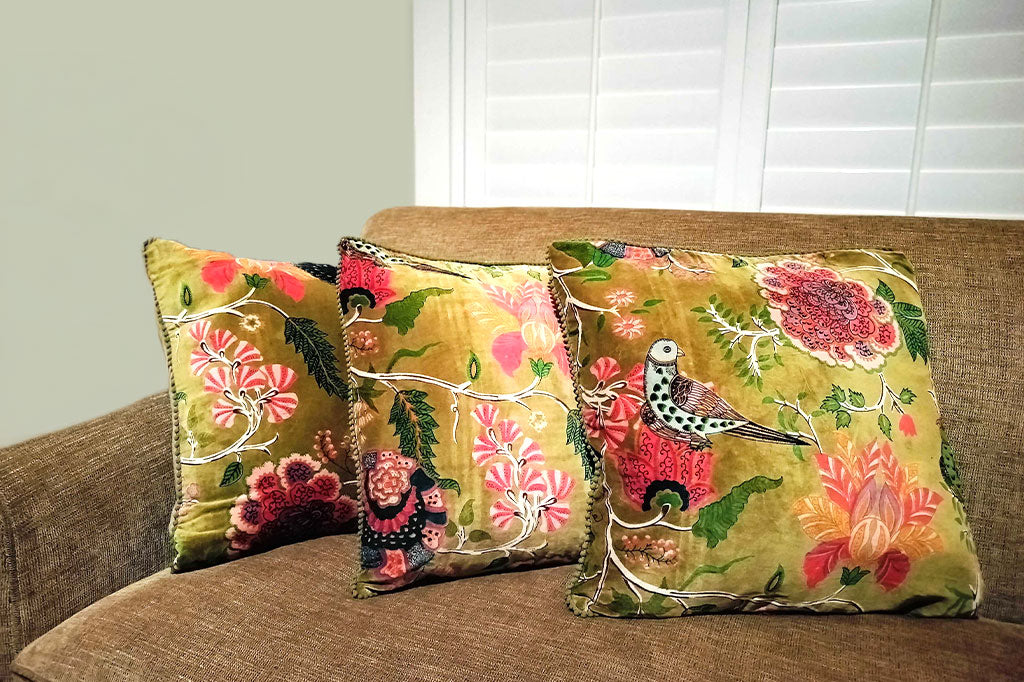 Decorative pillows with floral and bird patterns on a brown couch.