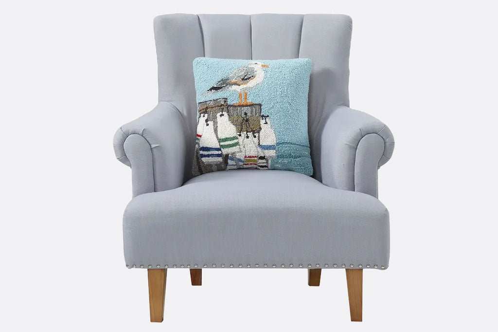 Featuring a seagull perched upon a buoy filled pier, a hooked wool throw pillow shown on gray love seat