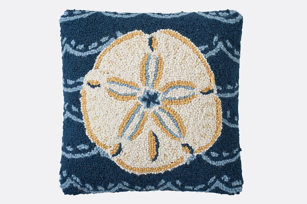 Hooked pillow featuring a cream colored sand dollar against a dark blue ocean with wave design 
