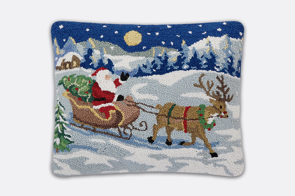 Decorative pillow with a Christmas scene of Santa Claus in a sleigh pulled by reindeer.