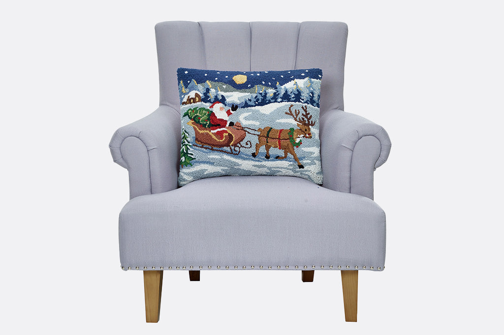 Gray armchair with a decorative pillow featuring Santa Claus and reindeer on a snowy background.
