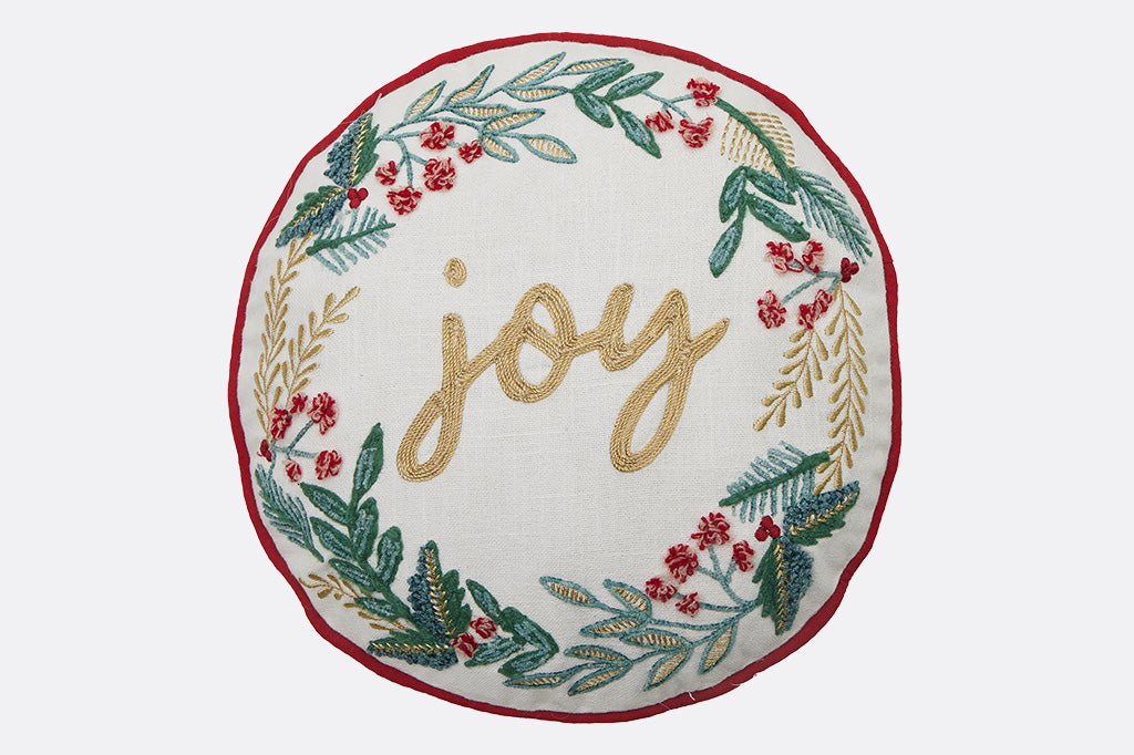 Decorative round pillow with 'joy' embroidery and festive wreath design on a white background