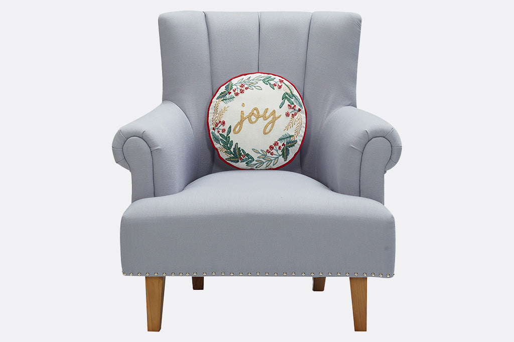 Gray armchair with a decorative pillow featuring the word 'joy' on a white background