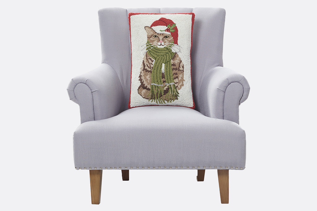 Vertical oriented throw pillow in hooked wool - shows a tabby cat in santa hat, staged on grey armchair on white background