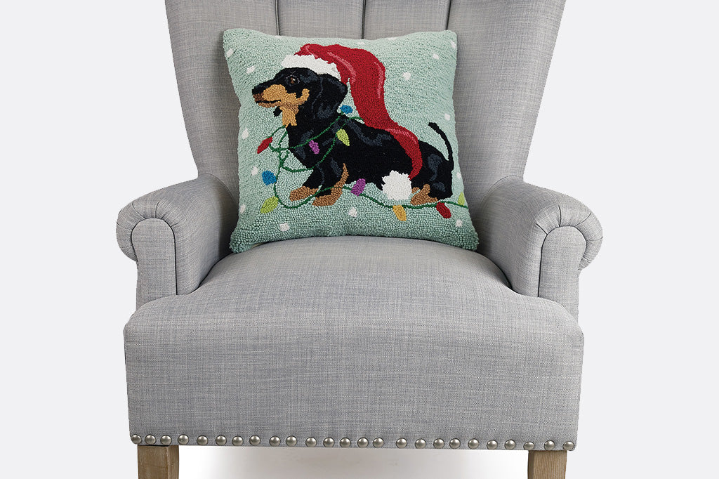 Decorative pillow with a Christmas-themed design of a dog wearing a Santa hat on a gray chair.