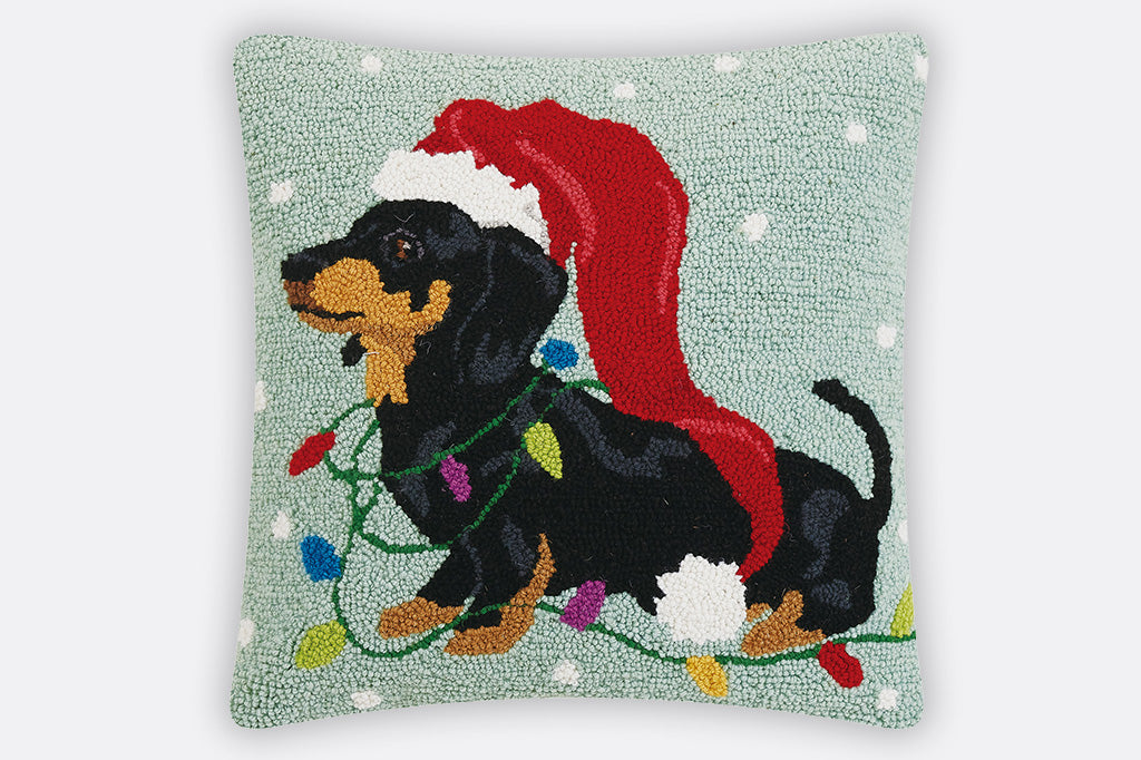 Decorative pillow with a dachshund wearing a Santa hat and surrounded by Christmas lights on a light green background.