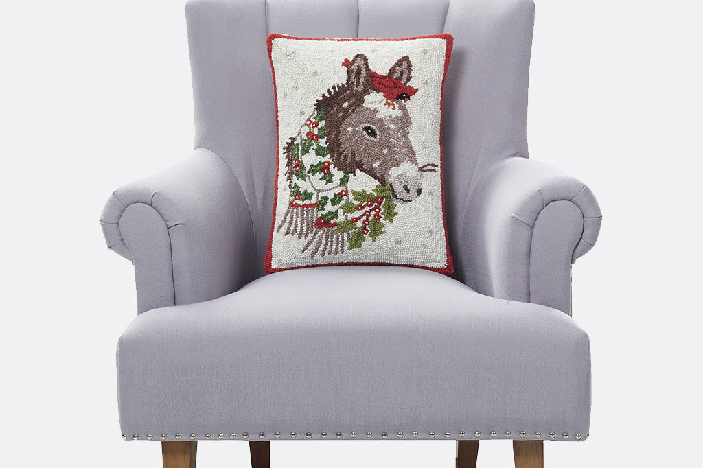 Decorative holiday hooked wool pillow with a burro design on a gray armchair