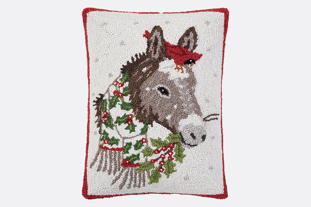 Decorative pillow with a donkey design wearing a scarf in the snow with white background. Cardinal sits on its head