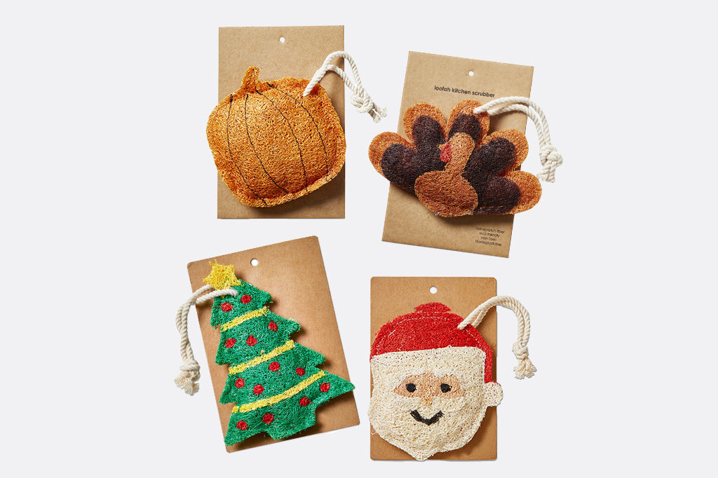 Four Autumn and Christmas-themed dish scrubbing loofahs on brown cards against a white background
