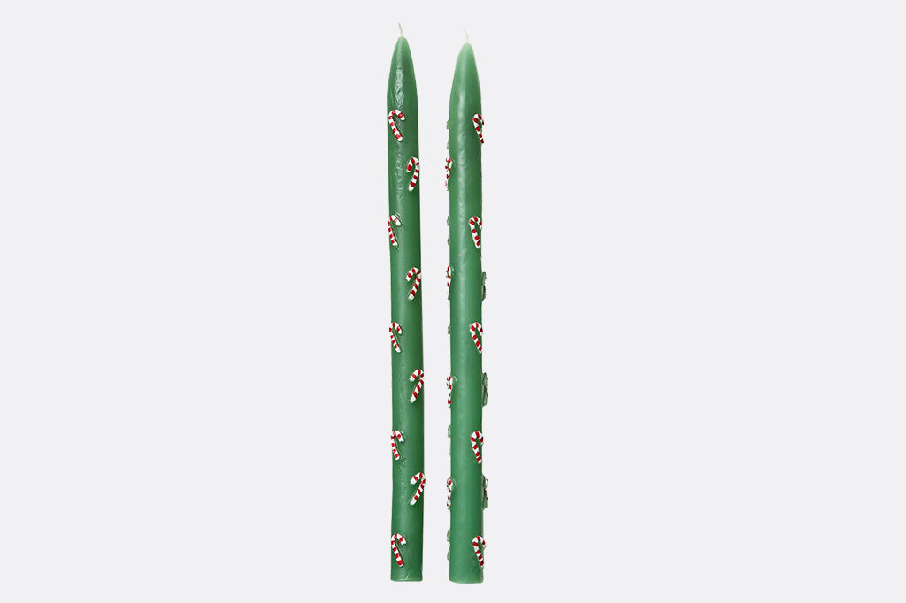 Two green candles with small decorative candycane elements on a light gray background