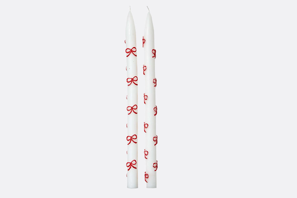 Two white candles with red bow designs on a white background