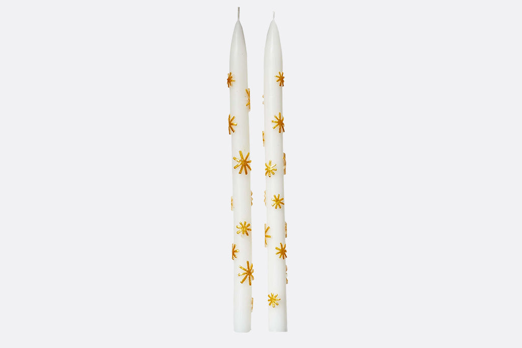 Two white candles with gold star patterns on a light gray background