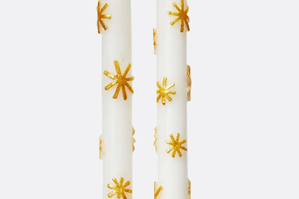 Two white candles with gold star designs on a white background