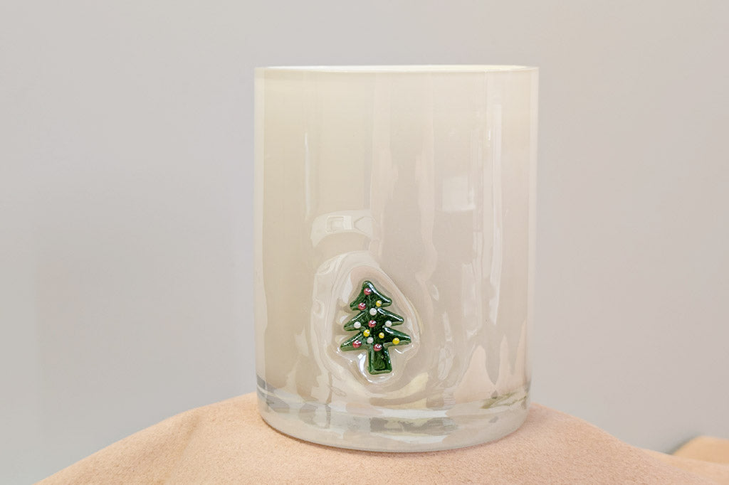 Glass candle with a Christmas tree design on a beige surface and light gray background