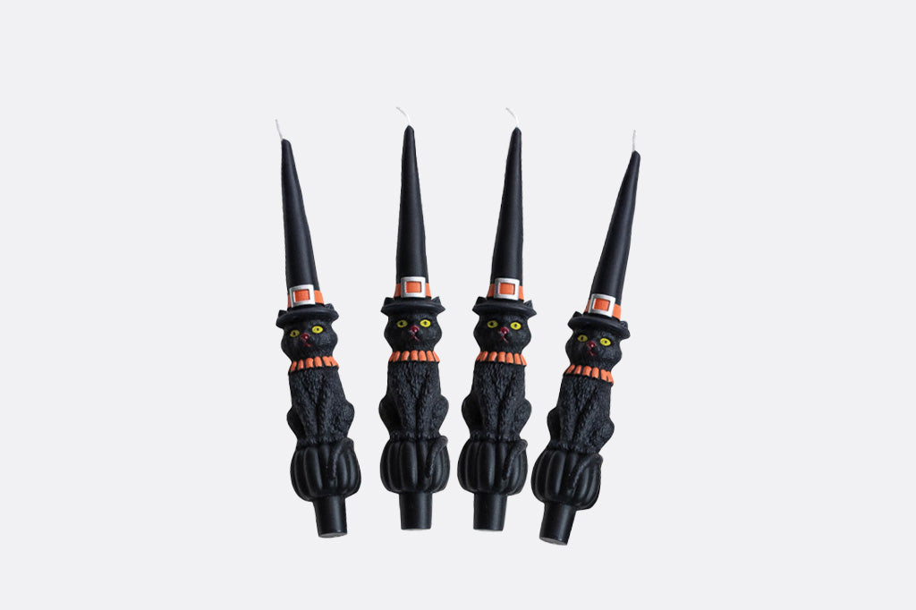 Four black witch candle holders with green eyes on a white background