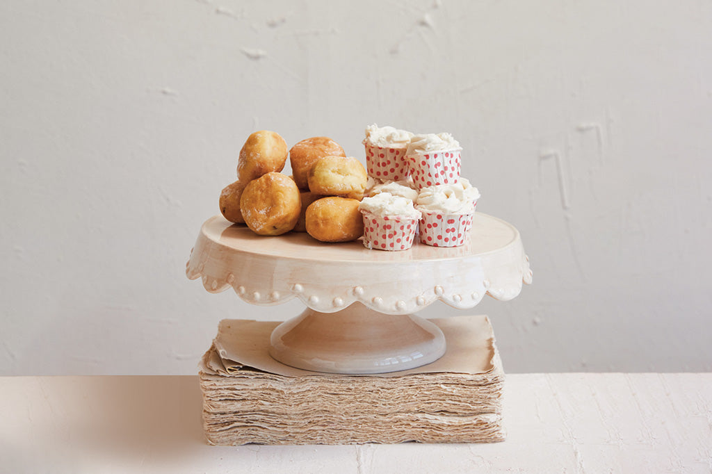 Cake stand with pastries and cupcakes balanced on a stake of vintage paper on a white surface